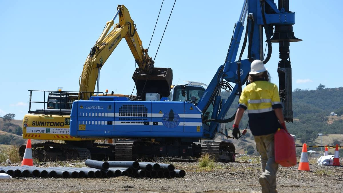 A crew member in high visibility workwear beside a drilling rig