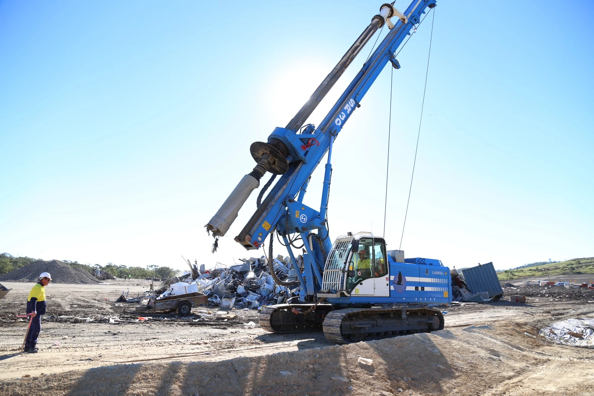 A blue drilling rig with its mast positioned on a landfill site