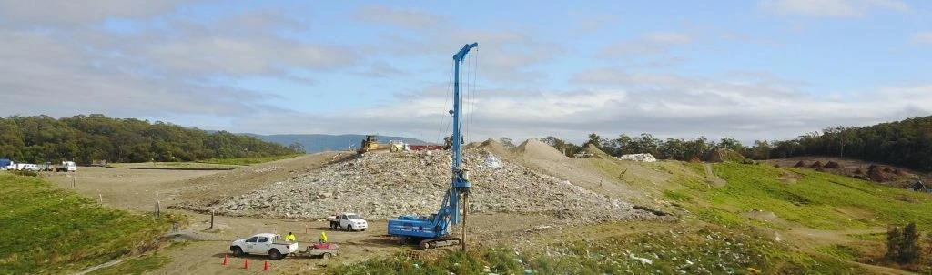 Wide view of a drilling rig on an Australian landfill, surrounded by green managed land